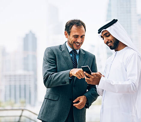 Emirati and Western businessmen checking content on smart phone. The man in white clothes is holding black smart phone.